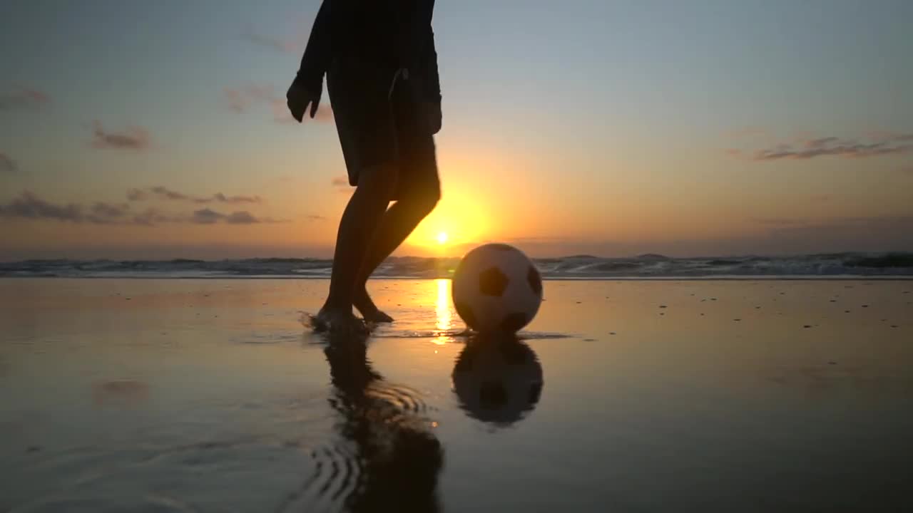 男孩在沙滩上玩球的剪影视频素材