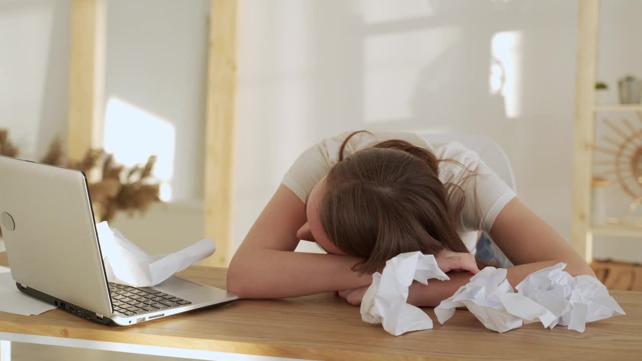 年轻疲惫的女人睡在她的办公桌旁边的笔记本电脑视频素材
