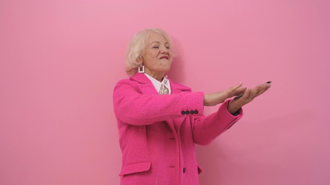 一个穿着时尚粉色外套的富有优雅的女人扔掉了钱，把它花在一个被粉红色背景隔开的无用的东西上视频下载