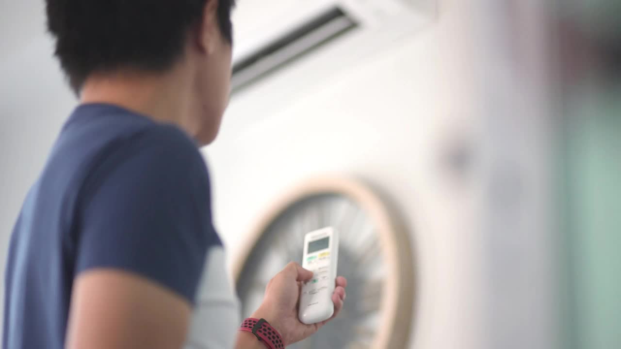 亚洲人正在用遥控器调节家里空调的温度视频下载