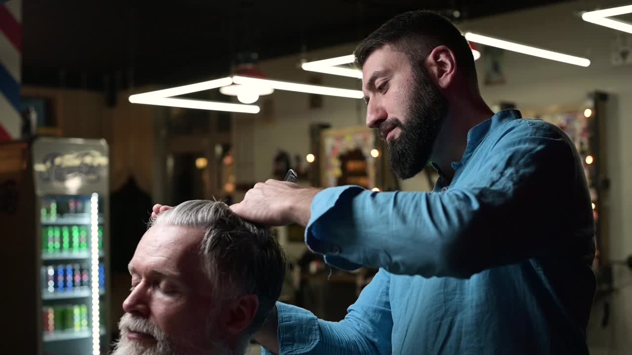 近距离的理发师在理发店里为一位白发苍苍的客户理发视频素材