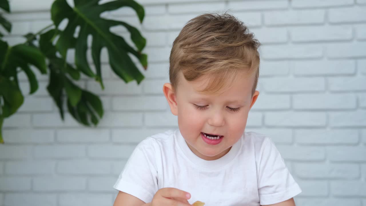 一个小男孩正在吃煎饼。快乐的孩子高兴地吃了一口煎饼。忏悔节。视频素材