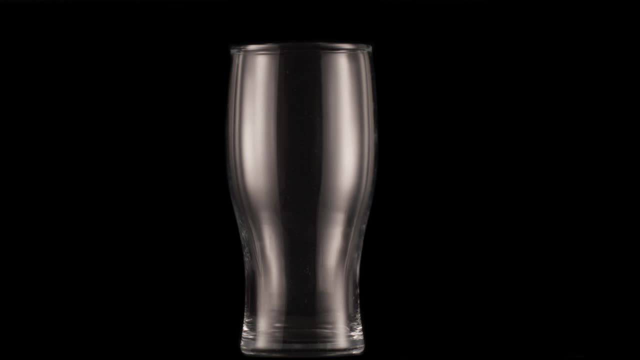 黑色背景下的一杯黑啤酒。一架喷气式飞机慢慢地将酒杯装满啤酒，造成大量的气泡和泡沫。视频下载