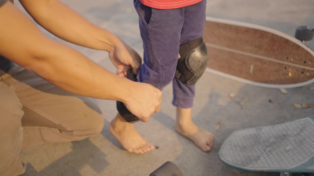 男子帮助孩子在滑板前戴上护膝。视频下载