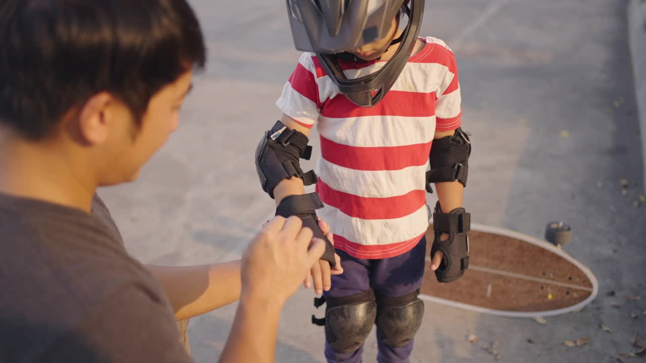 亚洲父亲检查防护手套，运动头盔和肘部保护他的孩子。视频素材