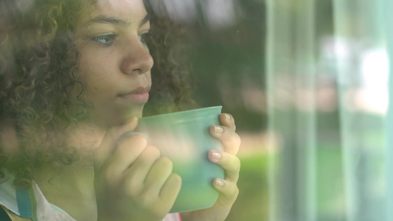 年轻女子在阳台门的玻璃后面喝咖啡视频下载