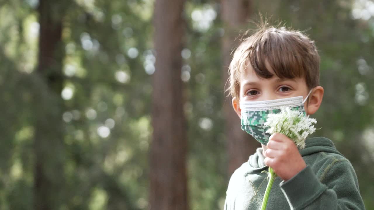 小男孩手持一束鲜花，戴着防护口罩视频素材