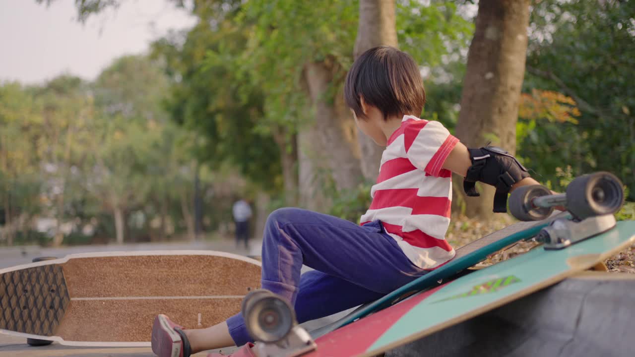 快乐的亚洲男生坐在滑板公园的滑板旁边。视频素材