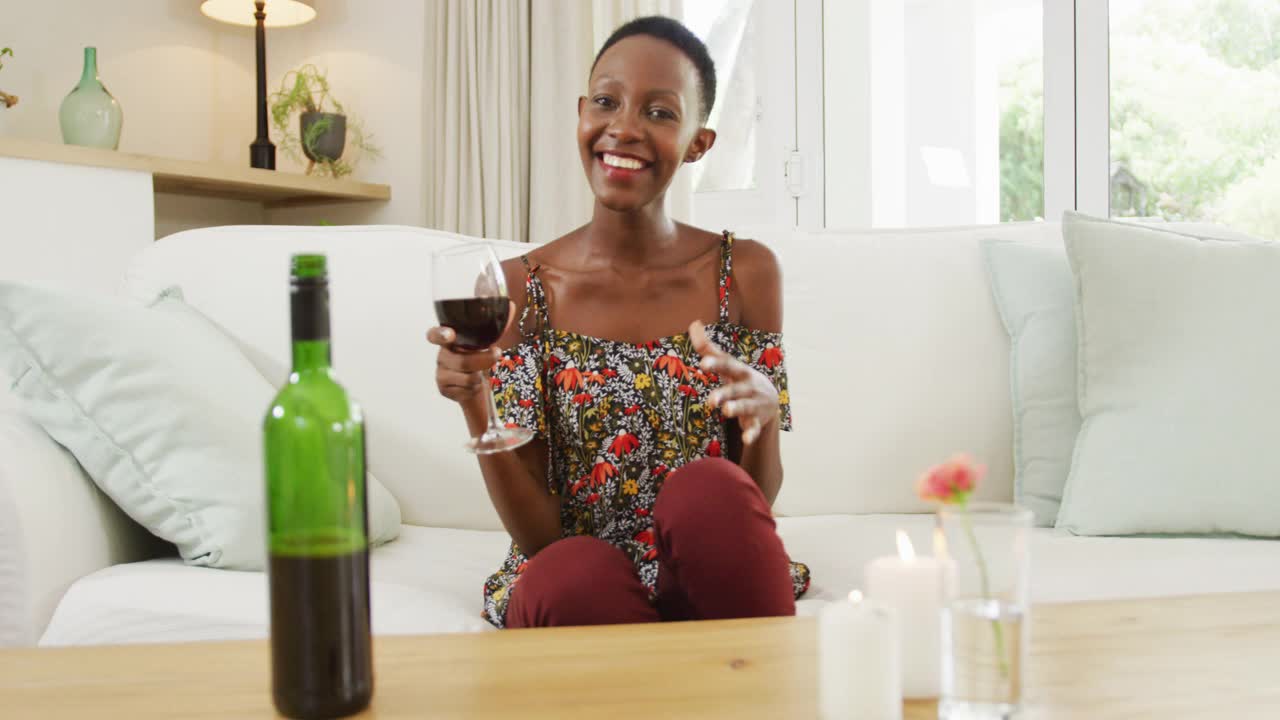 非裔美国妇女坐在沙发上举起酒杯，对着镜头微笑视频下载