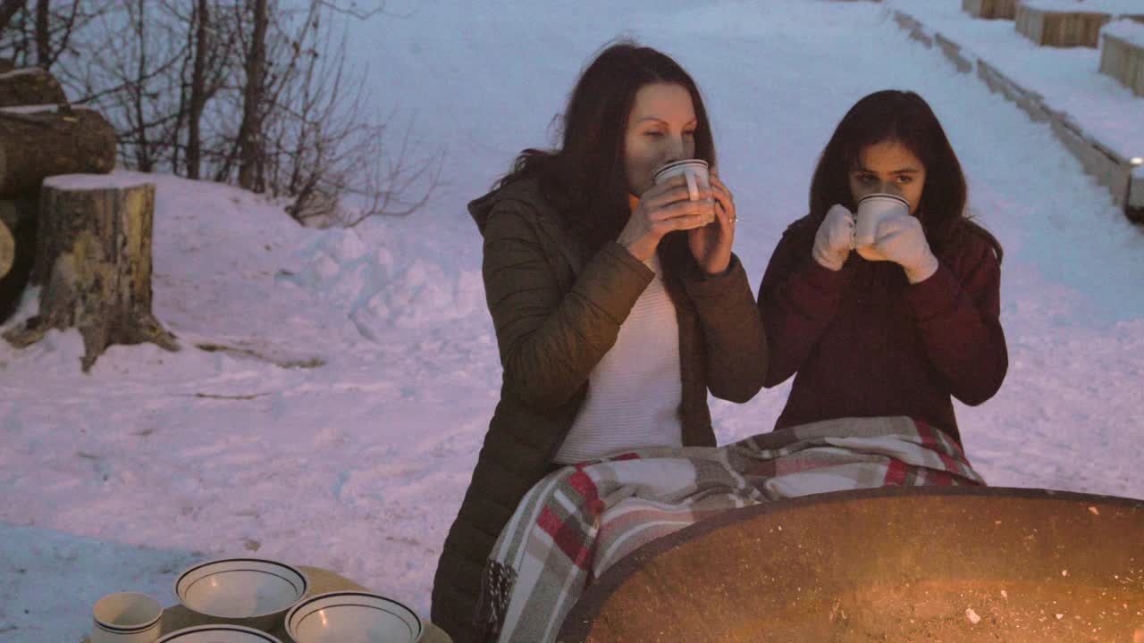 妈妈和女儿喝热巧克力旁边的冬季篝火视频下载