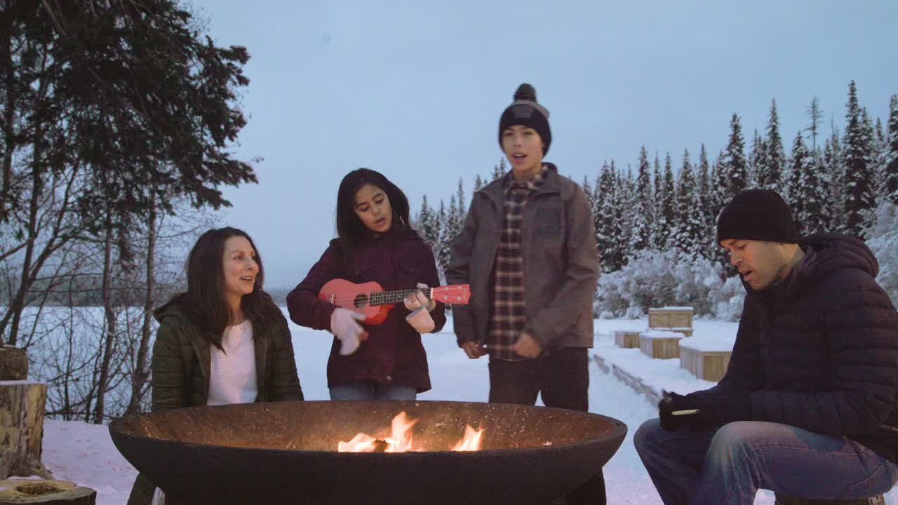 孩子们围坐在冬天的篝火旁弹奏尤克里里琴，家人一起唱歌视频下载