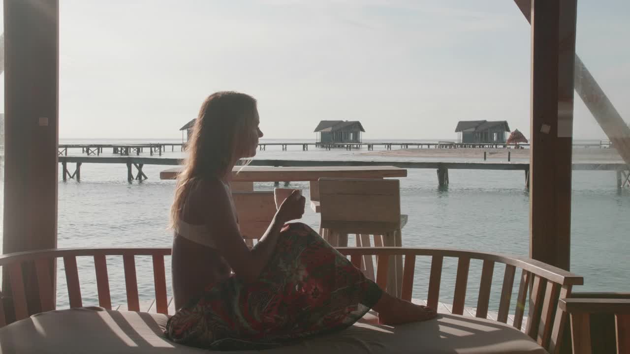 在一个酒店度假村的热带岛屿的咖啡馆里喝咖啡的女人。视频下载