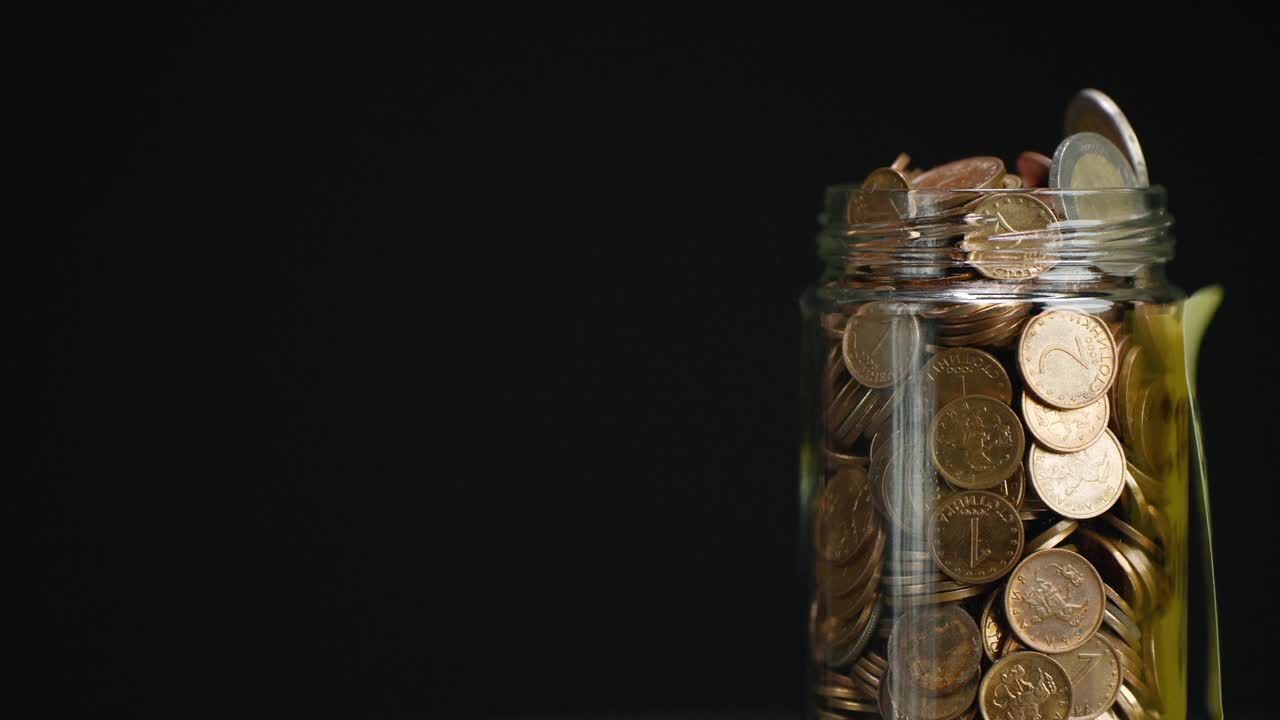 旋转玻璃罐装满硬币和两欧元硬币与粘贴的加密投资文本黑色背景，慢动作视频素材