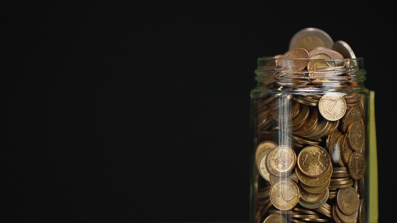 旋转玻璃罐装满硬币和两欧元硬币与粘贴的加密投资文本黑色背景的粘合剂注意视频素材