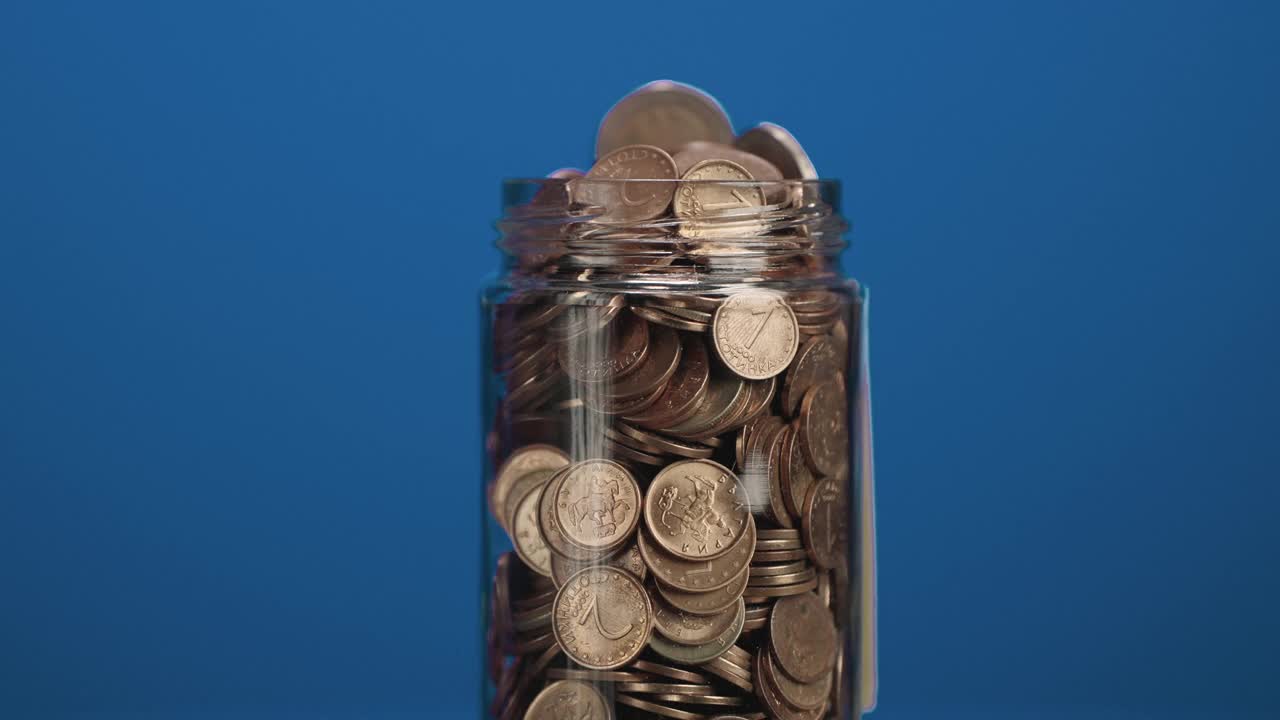 旋转玻璃罐装满硬币和两欧元硬币与粘贴的加密投资文本蓝色背景的粘合剂注意视频素材