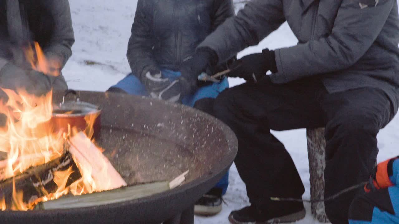 爸爸教儿子如何削木棒在火上烤蜜糖，而妈妈在一旁看着。视频下载