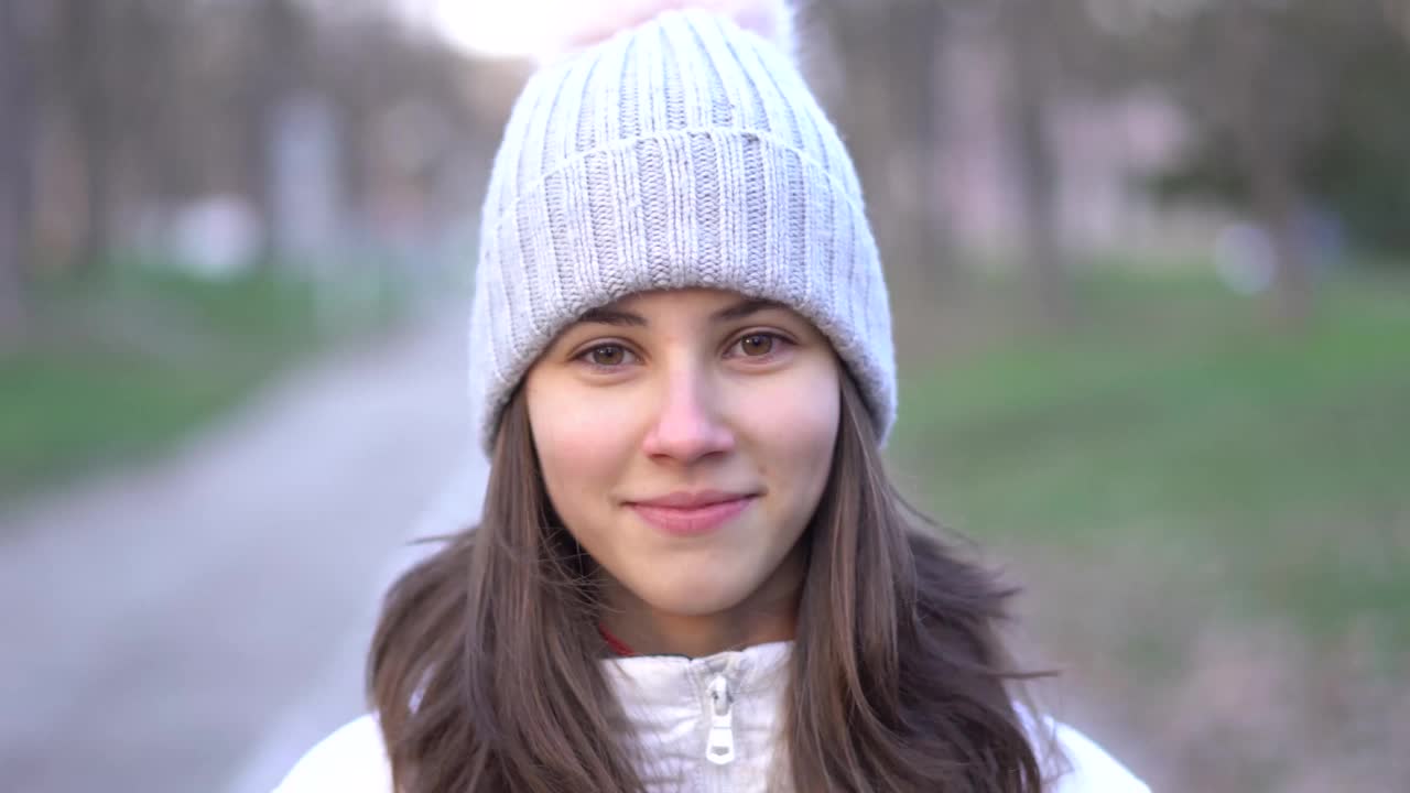 一个年轻女孩的肖像与针织帽站在一个公园视频素材