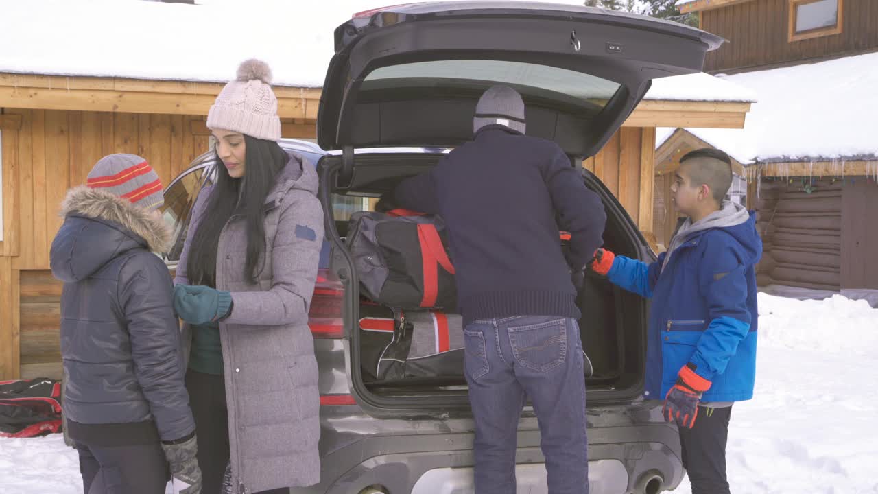 在寒假目的地，妈妈帮儿子穿上大衣，而另一个儿子帮爸爸卸车视频素材
