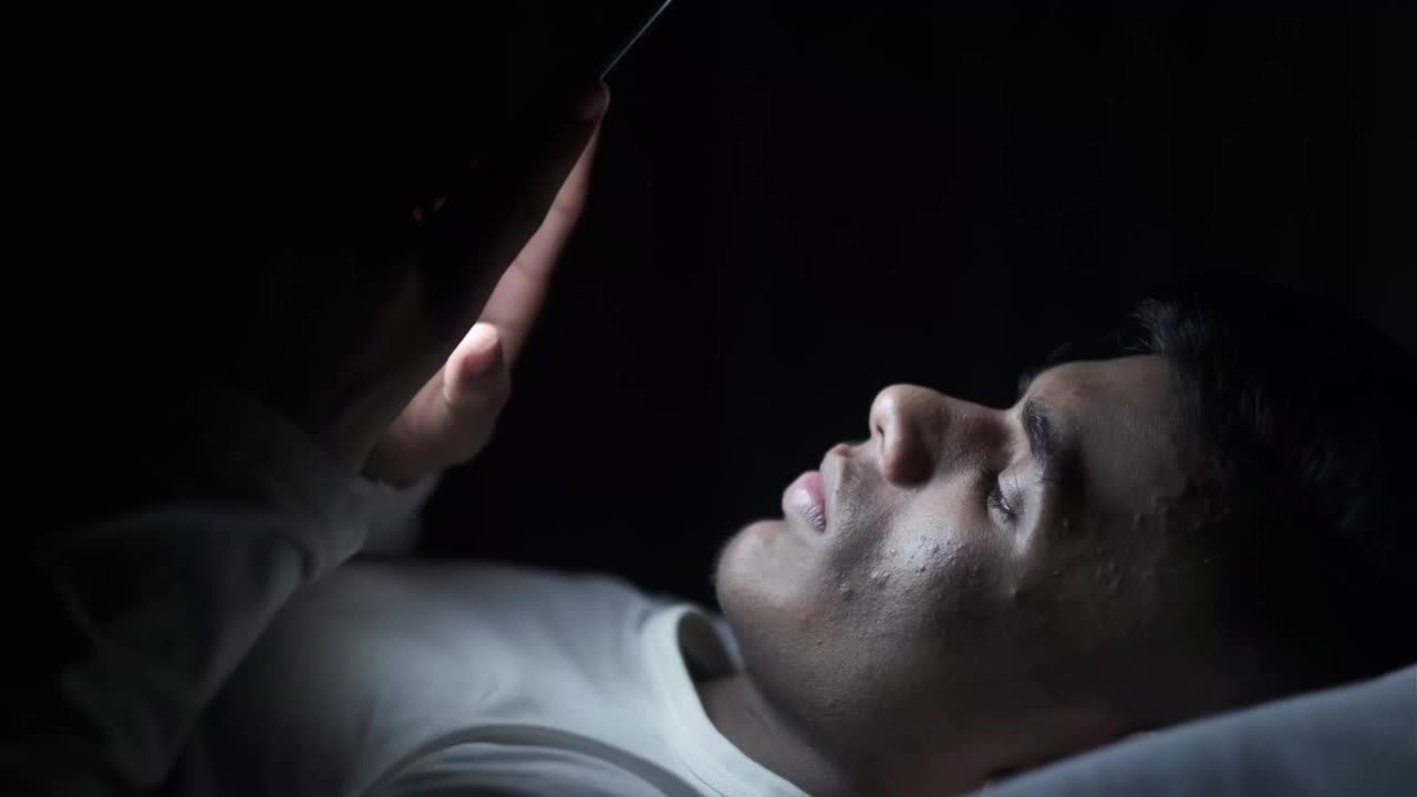 年轻人晚上在床上玩智能手机视频下载