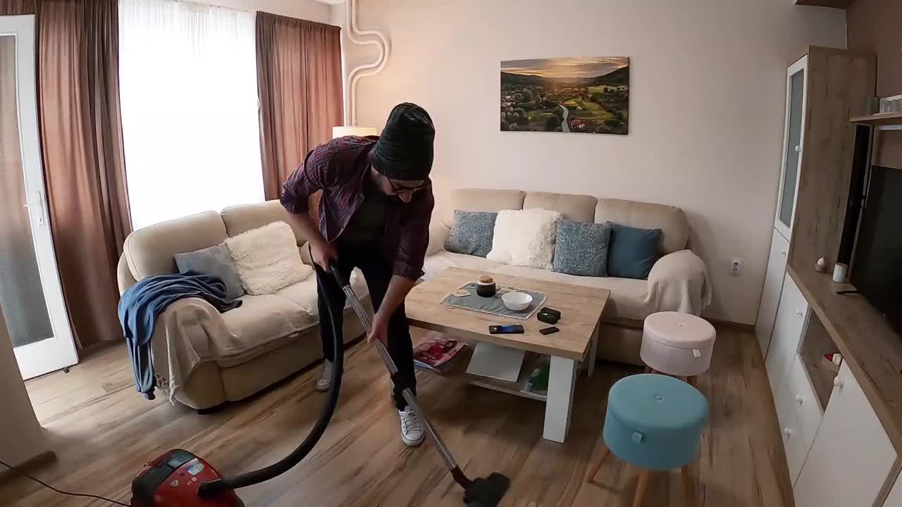 男人在家里拍自拍视频。一个快乐的男人穿着现代风格的衣服，一边用吸尘器打扫公寓，一边唱歌和玩耍。视频下载
