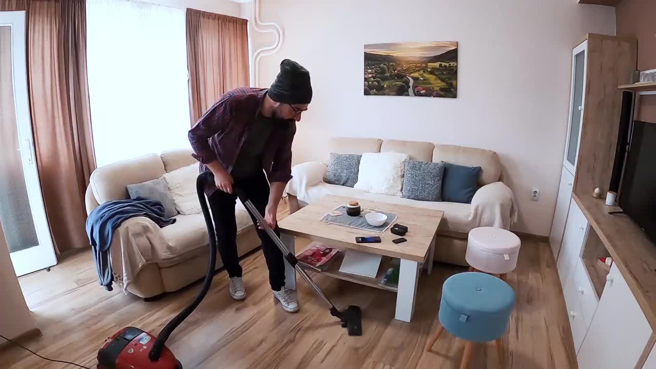 男人在家里拍自拍视频。一个快乐的男人穿着现代风格的衣服，一边用吸尘器打扫公寓，一边唱歌和玩耍。视频素材