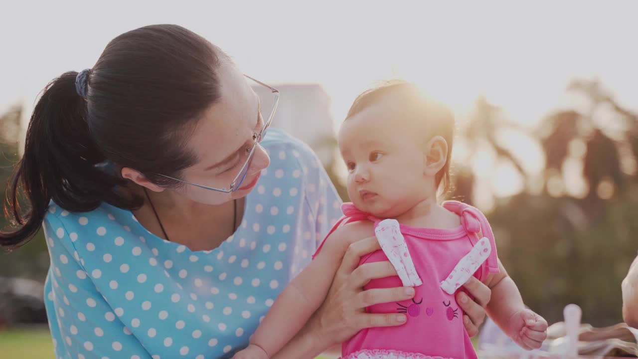 天真的亚洲婴儿享受和好玩的第一次在她的母亲的臂弯公园视频素材