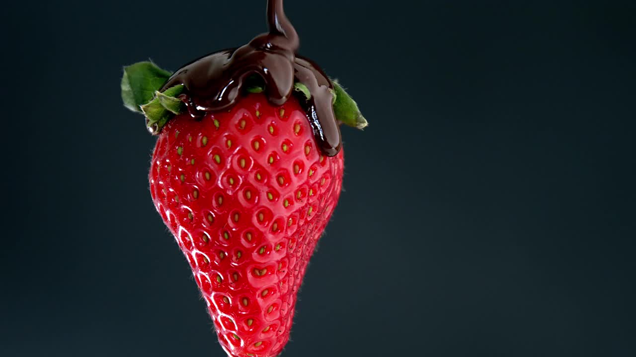草莓在黑色背景上旋转，上面覆盖着巧克力。视频下载