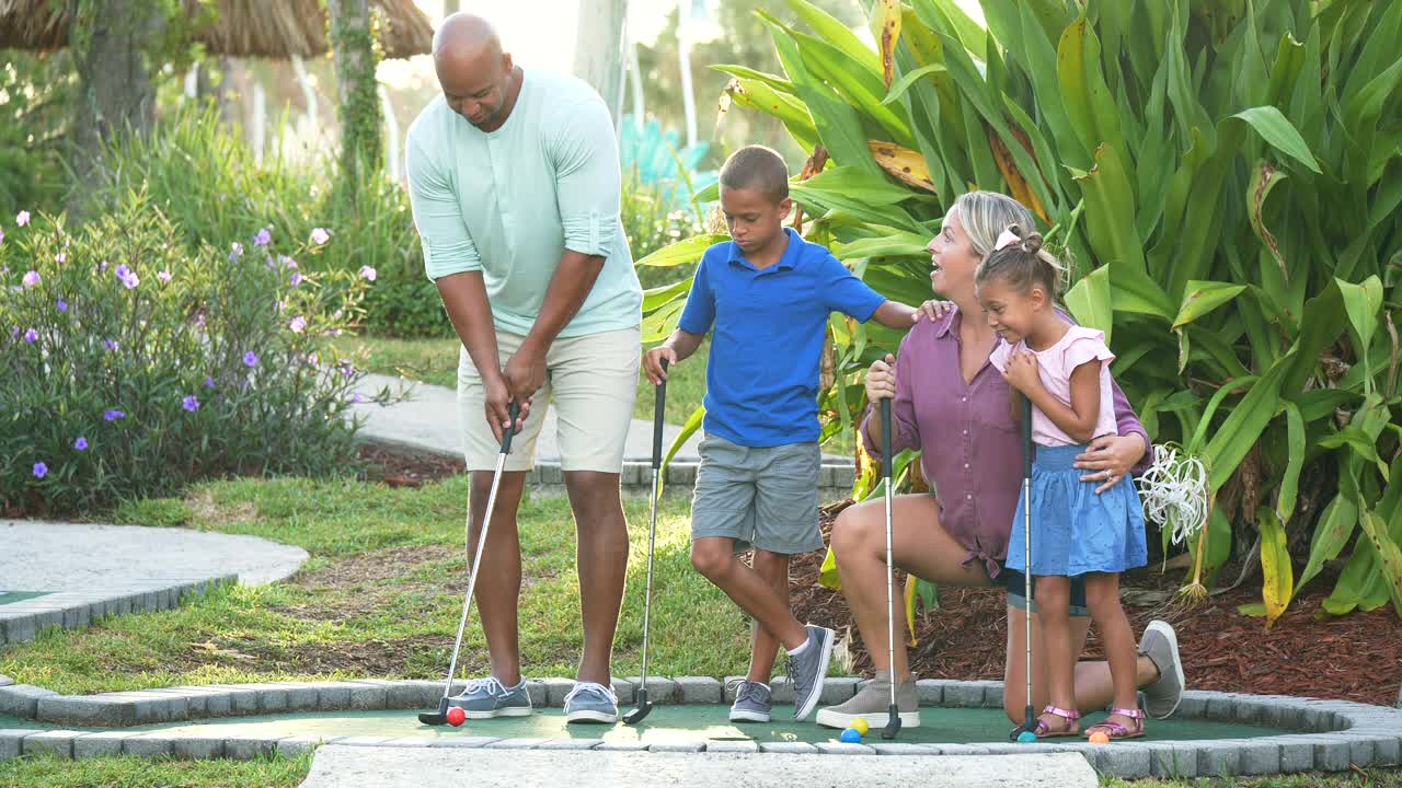 跨种族家庭，两个孩子打迷你高尔夫视频素材