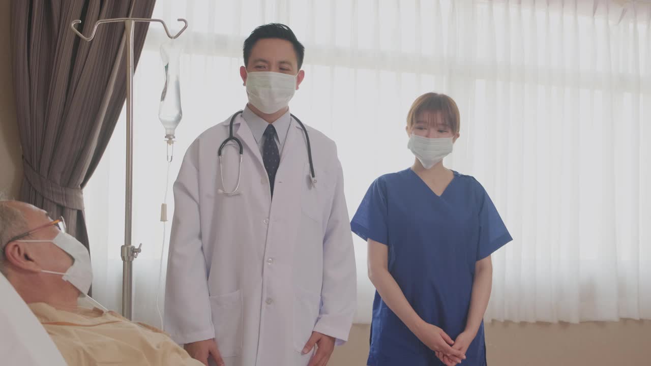 亚洲医生和护士用微笑鼓掌的方式鼓励躺在床上的病人。疫情大流行期间，患者和医护人员佩戴口罩预防感染。视频素材