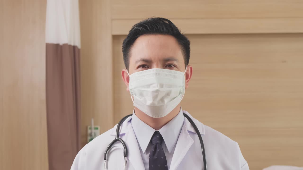 亚洲男医生戴上外科防护口罩，预防冠状病毒大流行。医护人员在医院穿医生袍戴口罩的肖像。健康职业新常态生活方式。视频素材