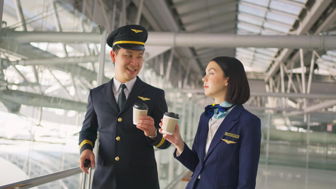 亚洲客机的飞行员和空姐在机场候机楼里微笑着一起喝咖啡。商务舱乘务人员或空姐，飞机和飞行员的职业概念。视频素材