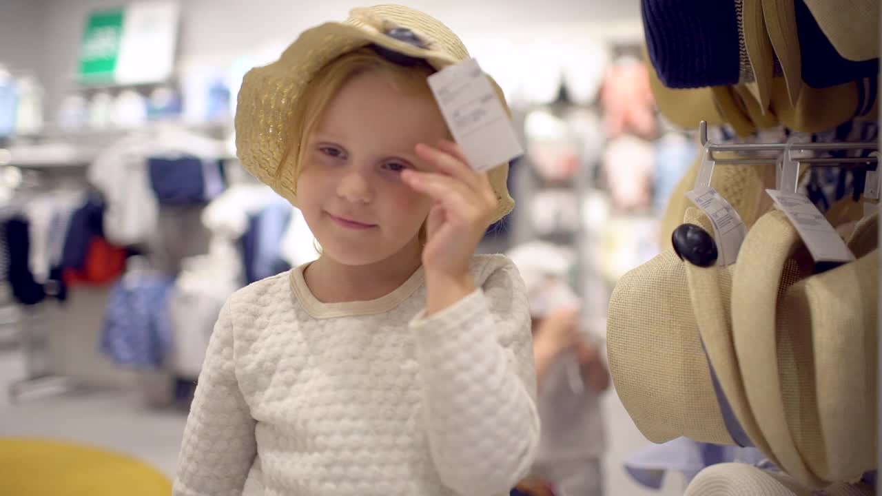 小女孩在超市挑选衣服。阖家欢乐购物。家庭购物中心。选择婴儿帽子视频素材