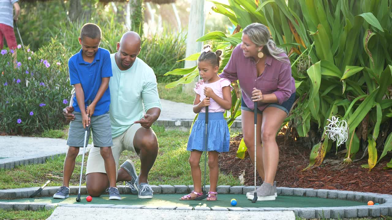 跨种族家庭，两个孩子在打迷你高尔夫视频素材