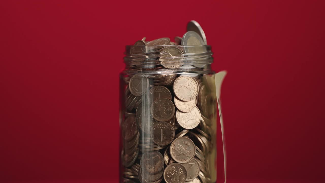 旋转玻璃罐装满硬币和两欧元硬币与粘贴的加密投资文字红色背景，慢动作视频素材