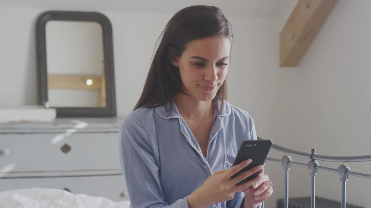 拿着手机的女人穿着睡衣坐在床上视频聊天视频素材