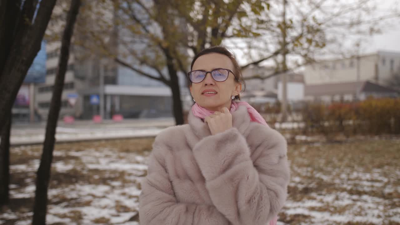 在城市里，一个穿着皮草大衣戴着墨镜的女人在镜头前摆姿势。冬天的肖像。视频素材