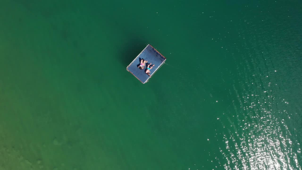 4K日光浴在绿松石湖浮动平台母子空中高空无人机俯视图。明亮的阳光反射在绿色的湖波中。克罗地亚达尔马提亚的佩卢卡湖视频下载