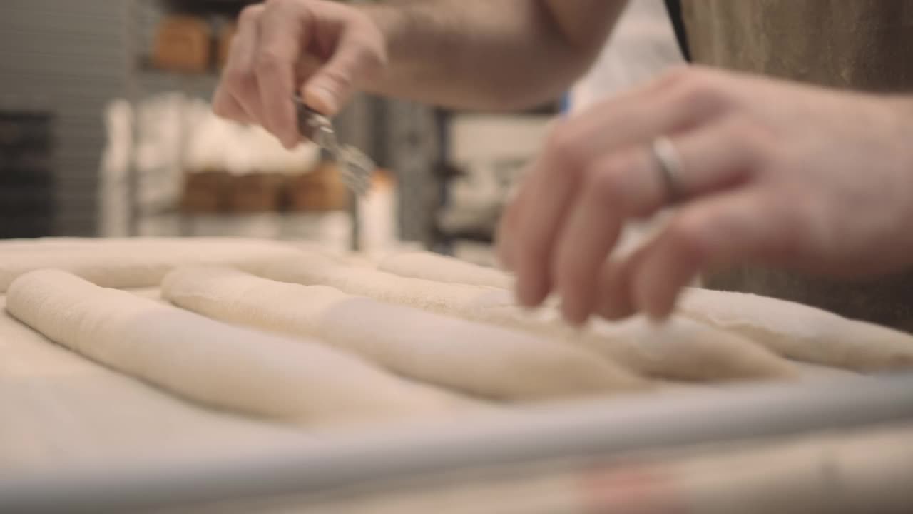 在工业面包房工作的蓄胡须的男性面包师正在为手工长棍面包准备面团视频下载