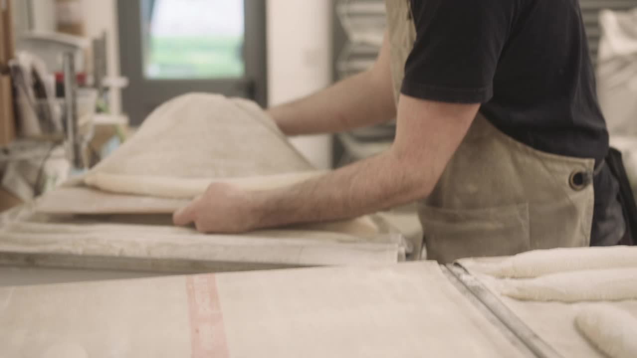 在工业面包房工作的蓄胡须的男性面包师正在为手工长棍面包准备面团视频素材