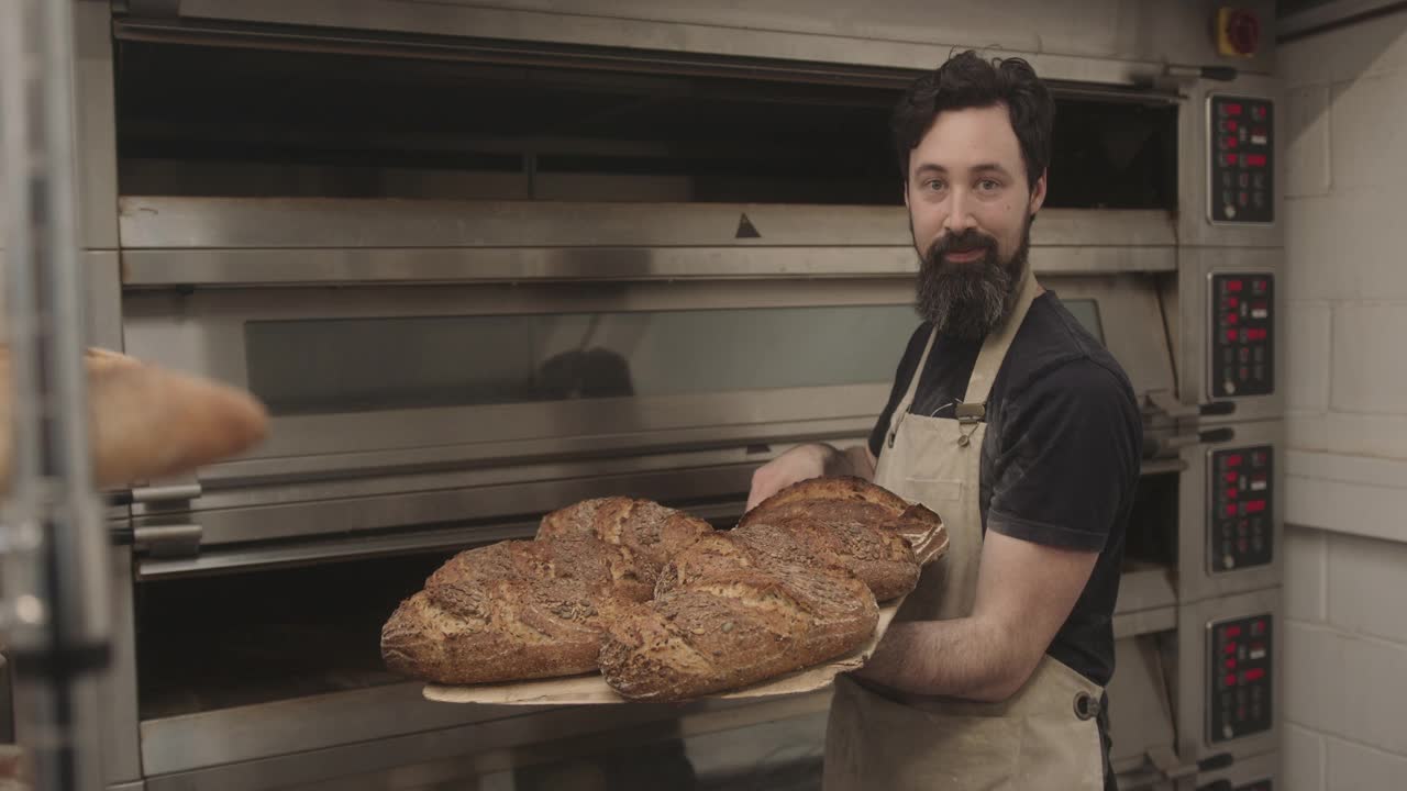 胡子男面包师把新鲜的酸面包从烤箱里拿出来的肖像视频素材