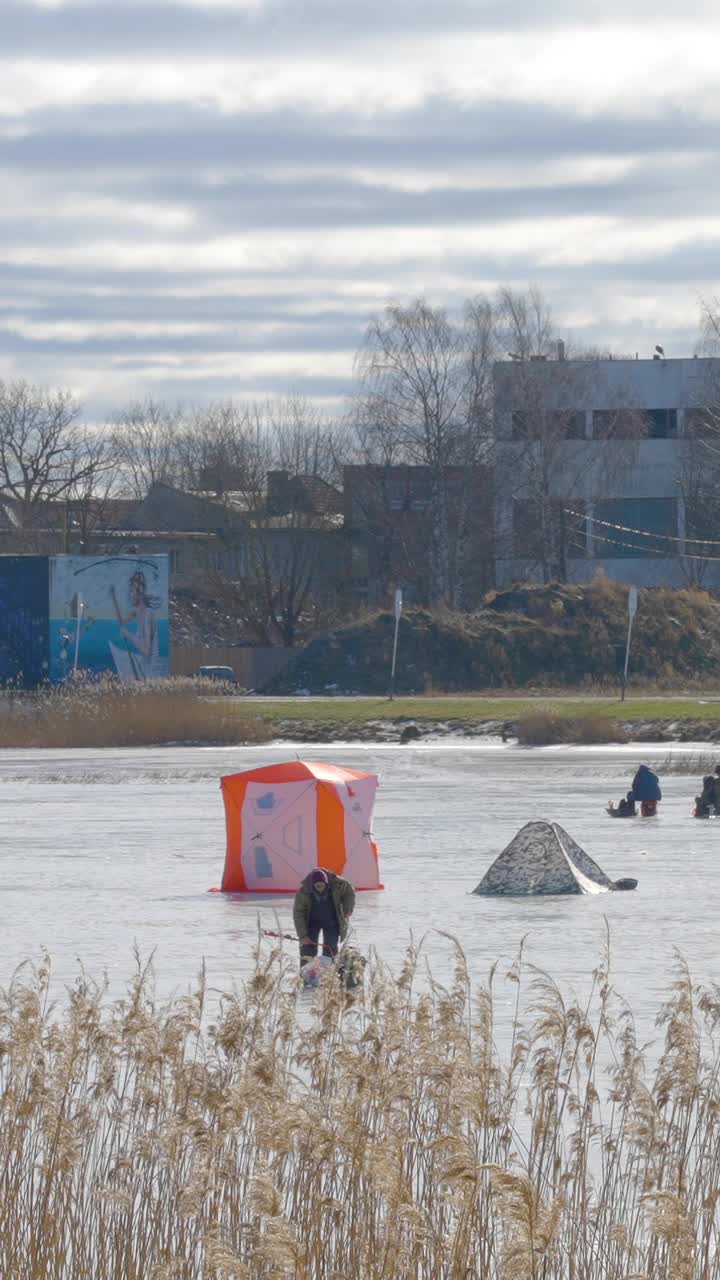 在爱沙尼亚的垂直视频中，人们在冰冻的水面上钓鱼视频素材