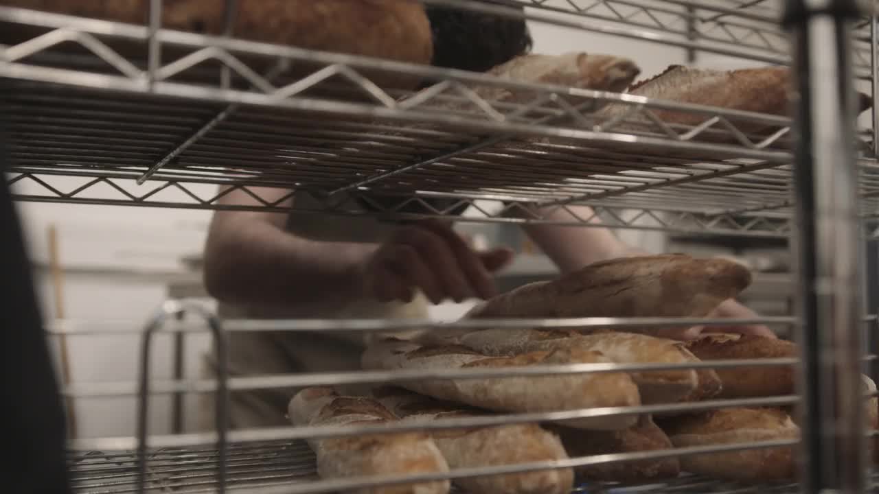 长着胡子的男面包师，穿着围裙在面包房工作，为外卖包装法棍面包视频素材