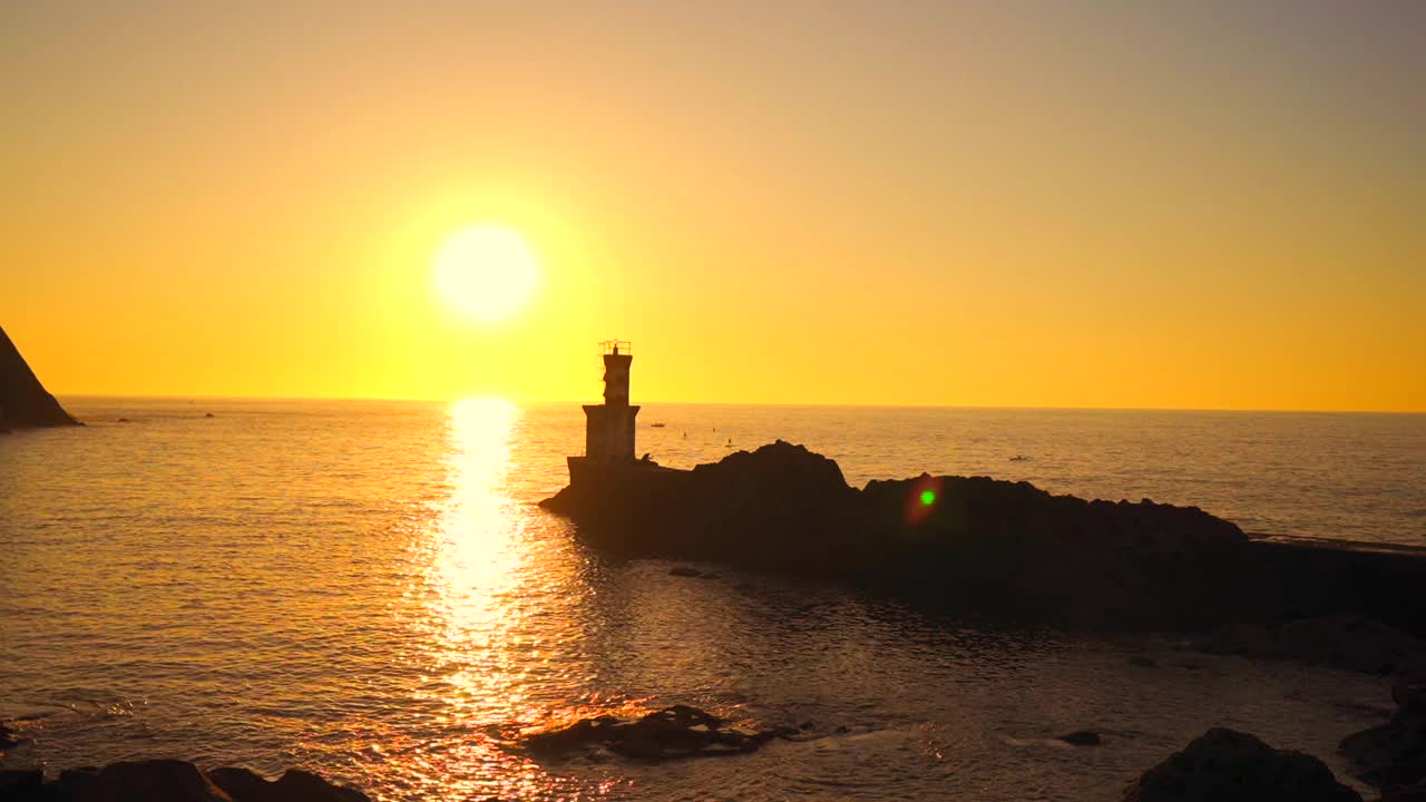 生活方式，一个戴着太阳镜的年轻人在日落旁边的灯塔坐在海边的岩石上。在夕阳下抽着烟视频下载