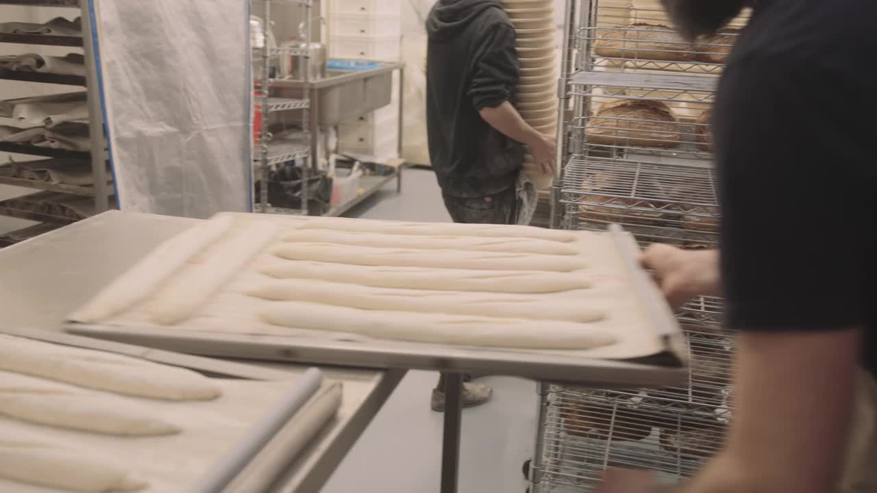 长胡子的男面包师正在把手工法棍放在烤箱里，在工业面包房工作视频素材