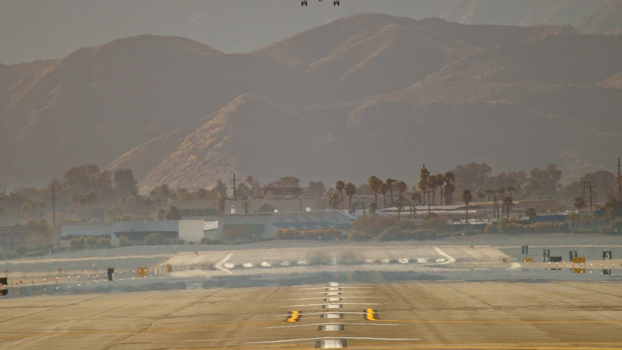 在棕榈树和沙漠山脉的背景下，喷气式客机在降落在机场跑道前缓慢下降的极端长镜头视图视频素材