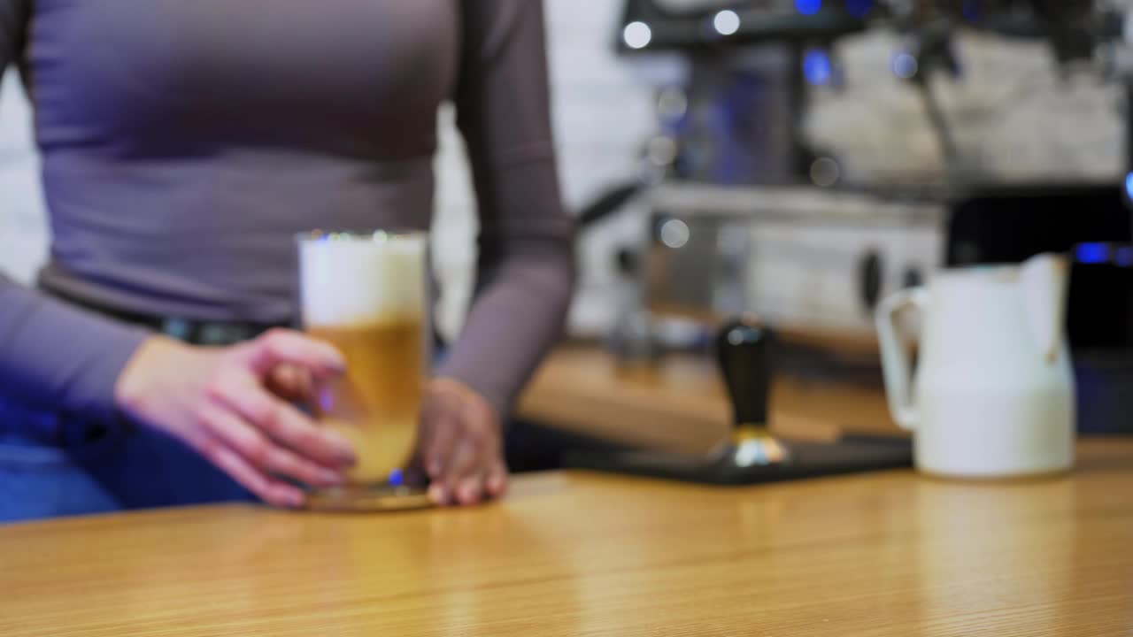 一杯卡布奇诺或拿铁。女人从咖啡机里拿出饮料。新鲜的咖啡和鲜奶油放在高脚杯上。特写镜头。视频素材