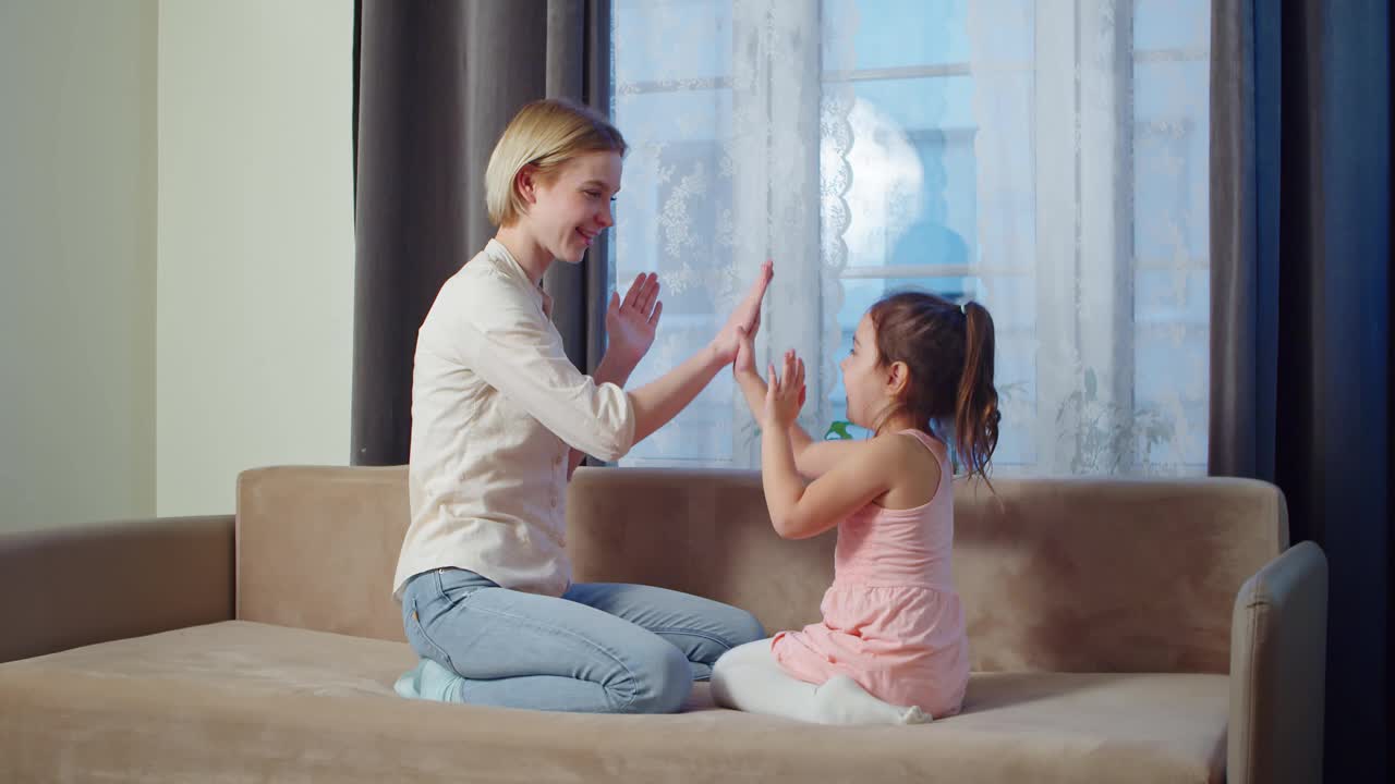 快乐的年轻妈妈和她的学龄前的女儿在沙发上玩视频下载