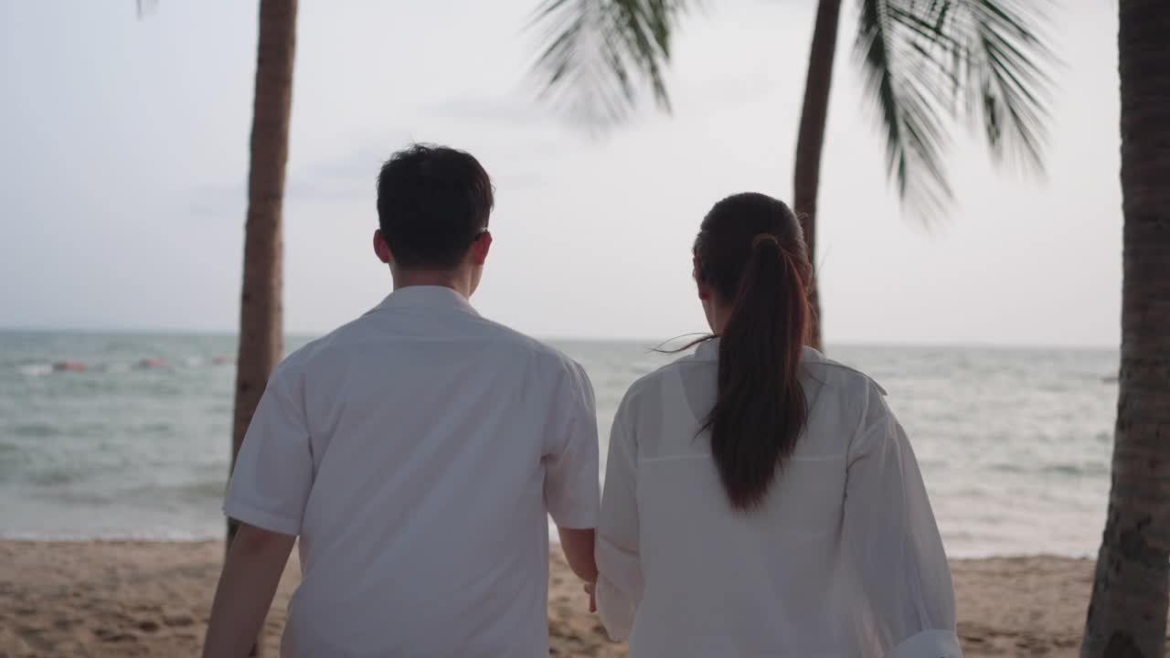 一对亚洲夫妇在泰国的一个有椰子树的海滨海滩上跑步和拥抱，此时正值夏天。视频素材