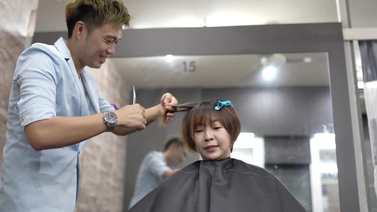 亚洲华人男性美发师在美发厅为女性理发。视频素材