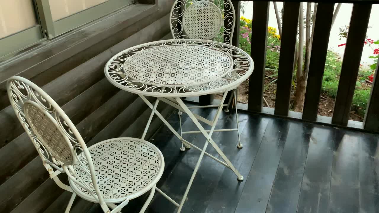两把白色金属椅子和一张棕色木制露台上的小圆桌。视频素材